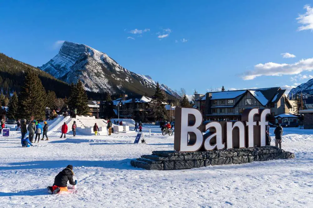 People enjoy outdoor activities in a snowy landscape with a large "Banff" sign in the foreground and Alberta's majestic mountains in the background, showcasing one of the top things to do in this winter wonderland.