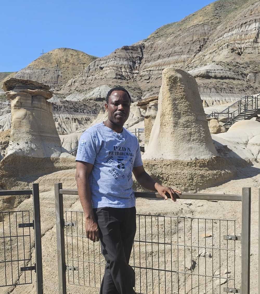 A person standing by a metal fence in front of unique rock formations in a desert landscape encapsulates the essence of our journey. Learn more about us and the adventures that define us.