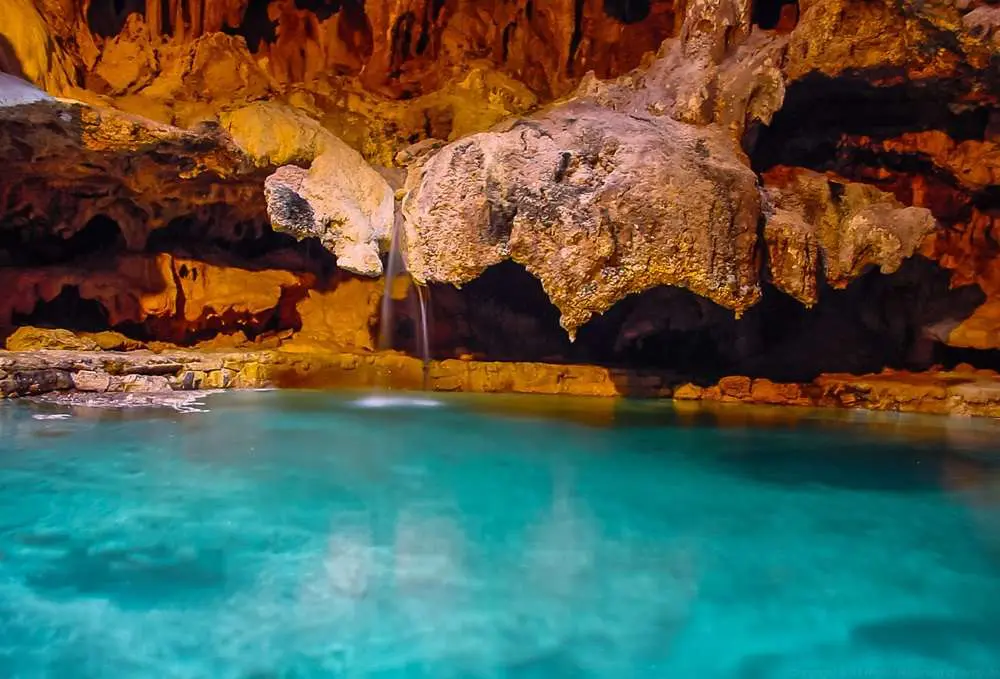 A small waterfall trickles into a turquoise pool inside a cave, surrounded by stalactites and rock formations, making it a must-visit spot for nature enthusiasts in Banff, Alberta.