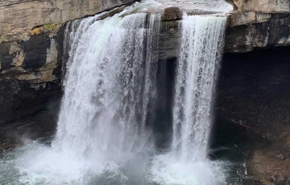 A waterfall flows over a rocky ledge, creating two main cascades side by side, with mist rising from the pool below. This is one of the stunning Alberta waterfalls that attract nature enthusiasts year-round.